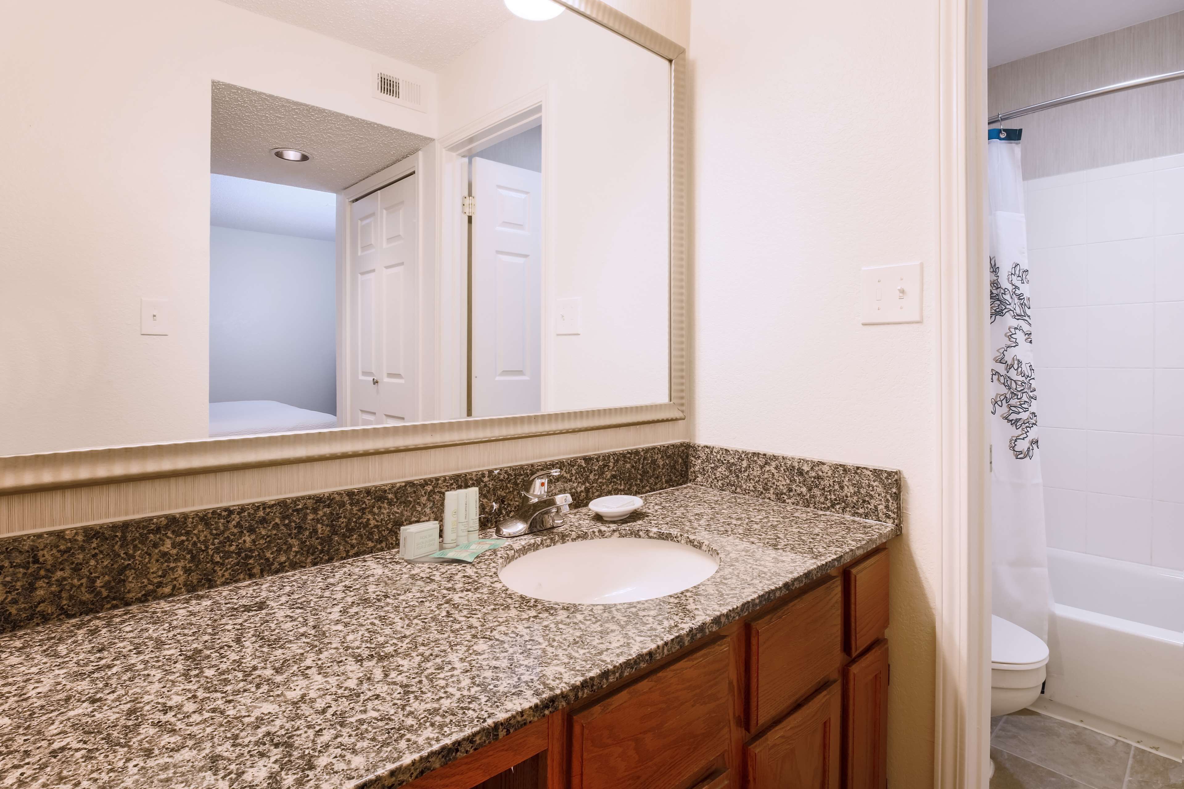 Une salle de bain avec un lavabo sur un plan de travail en granit, des meubles en bois, un grand miroir et un rideau de douche.