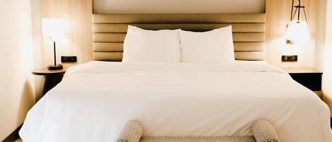 A hotel room with a large bed, two bedside tables with lamps, and a small bench at the foot of the bed.