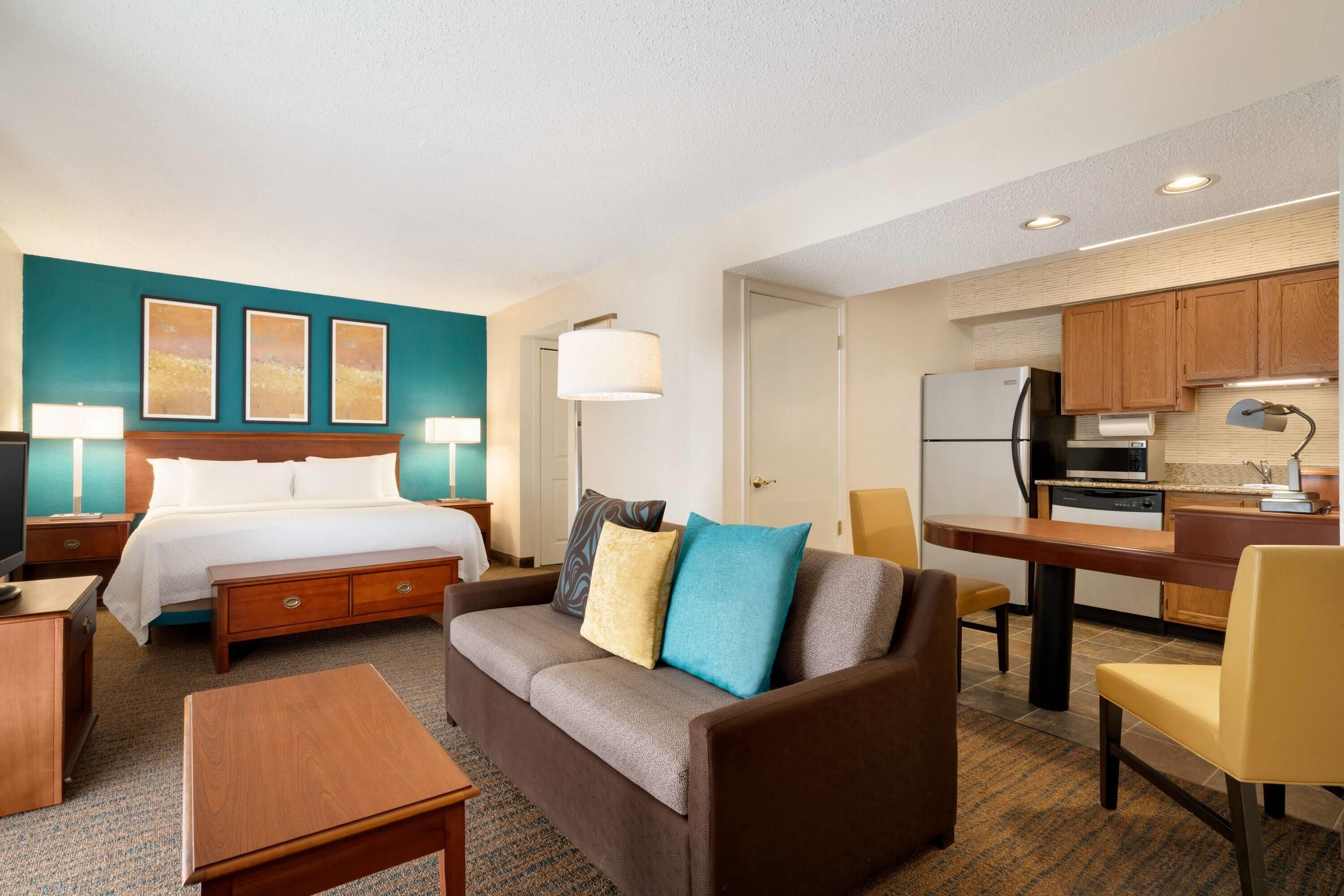 A hotel room with a bed, a sofa, a dining table, and a kitchenette.