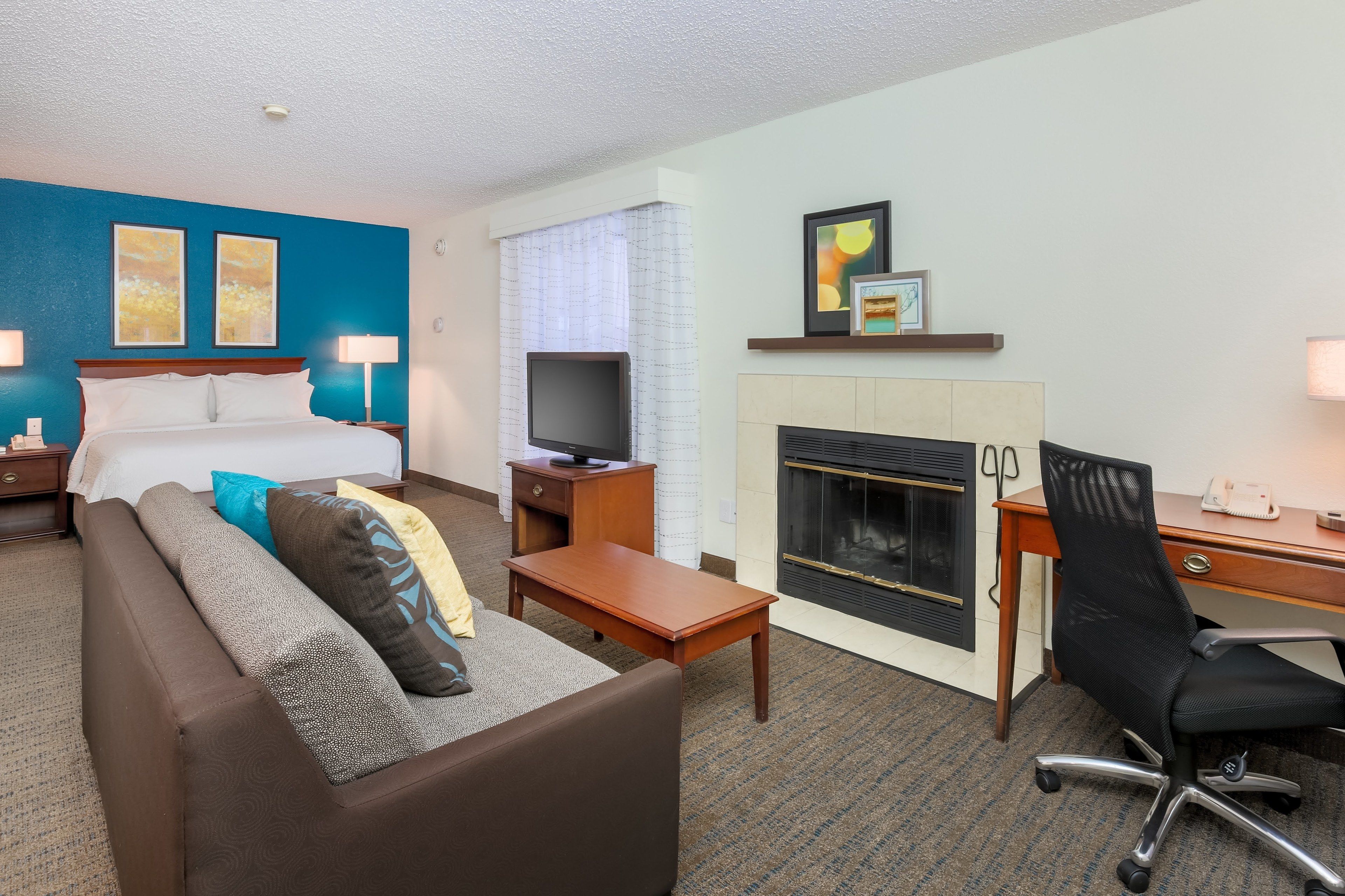 A hotel room with a bed, a TV, a fireplace, a desk, and a sofa.