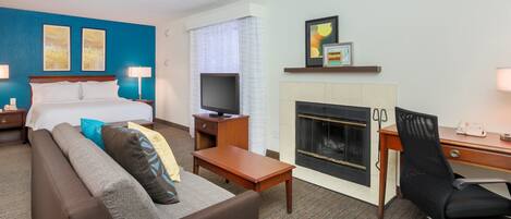 A hotel room with a bed, a TV, a fireplace, a desk, and a sofa.