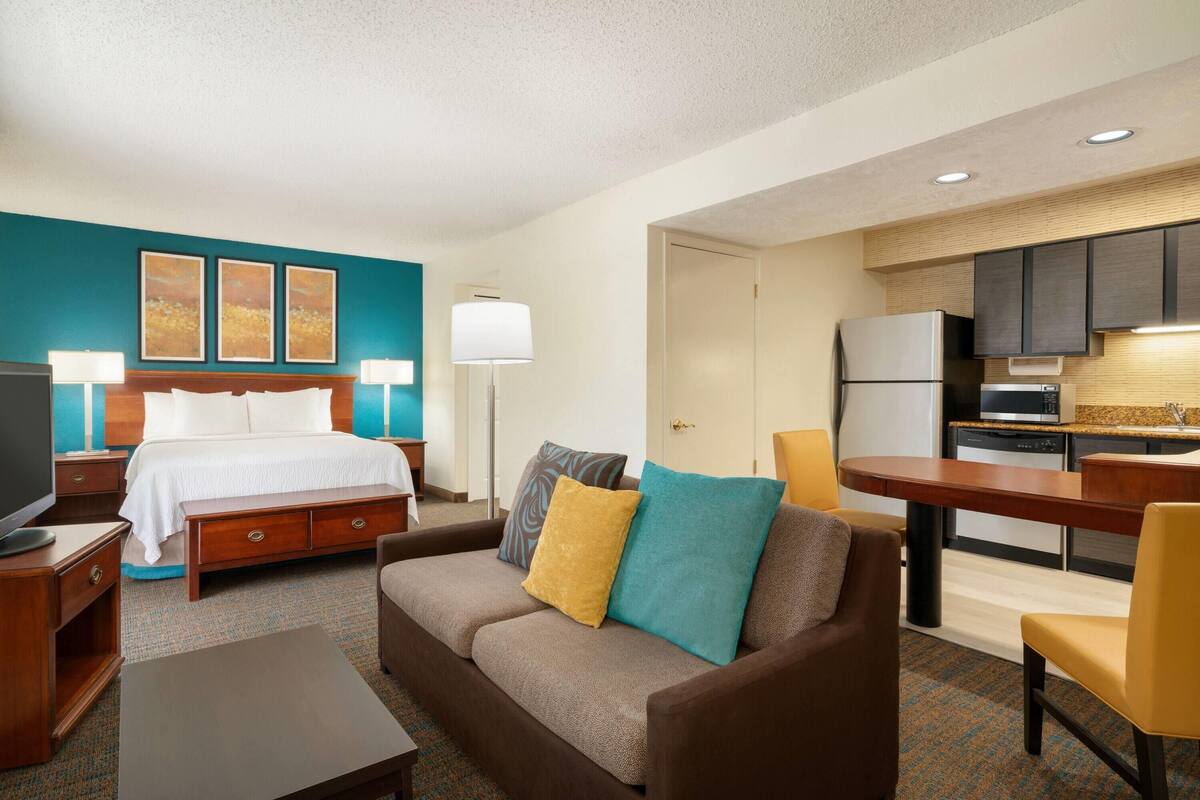 Habitación de hotel con cama, sofá, televisión, escritorio y kitchenette.
