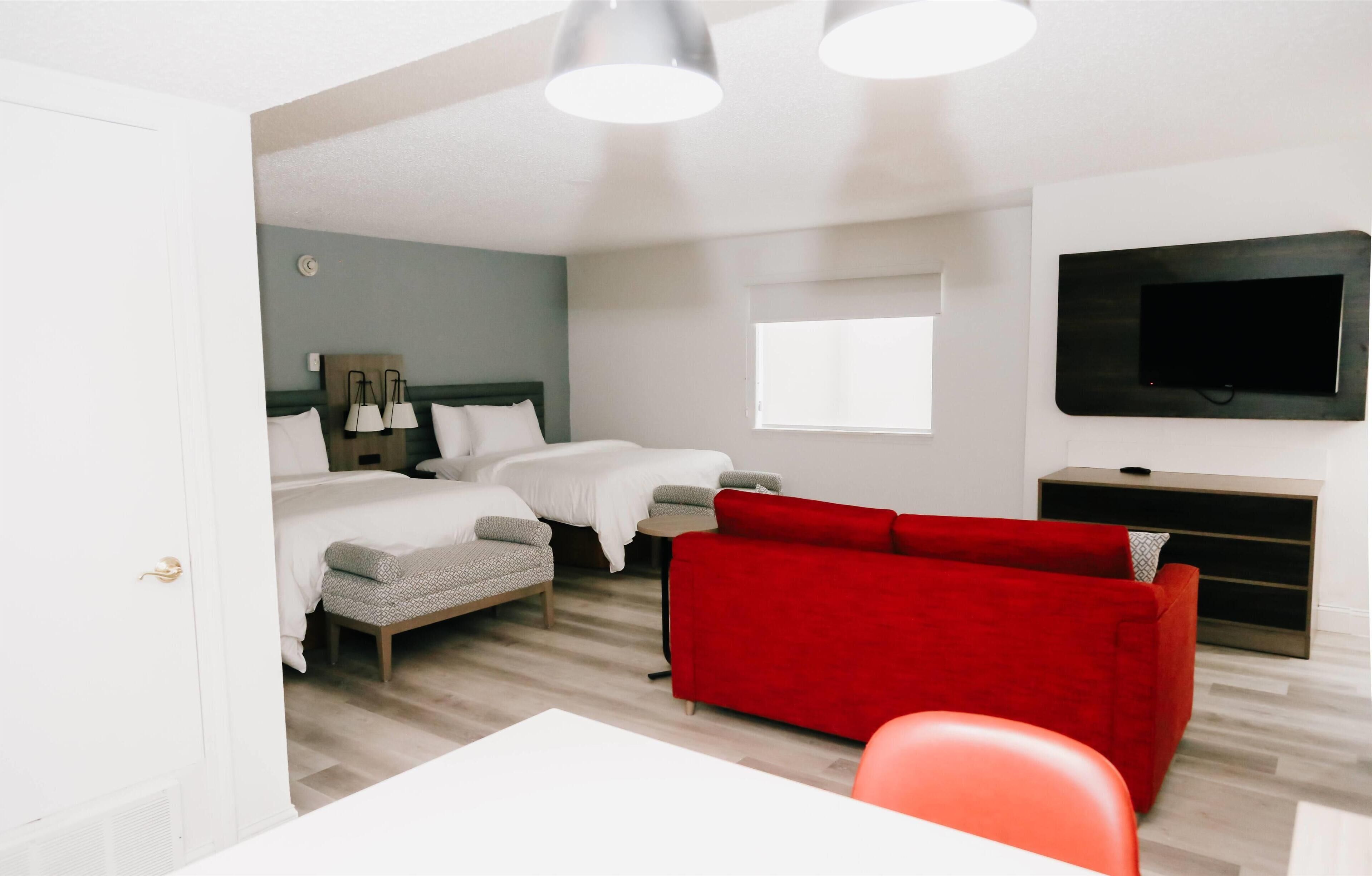 A hotel room with a bed, a red sofa, a TV, and a desk.