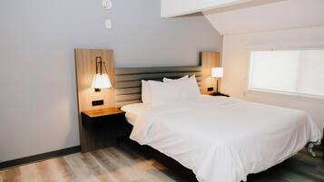 Una habitación de hotel moderna con una cama grande, dos mesitas de noche con lámparas, un cabecero de madera y un ventanal amplio.