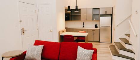 A compact living space with a red sofa, a dining table, a kitchen area, and a staircase.
