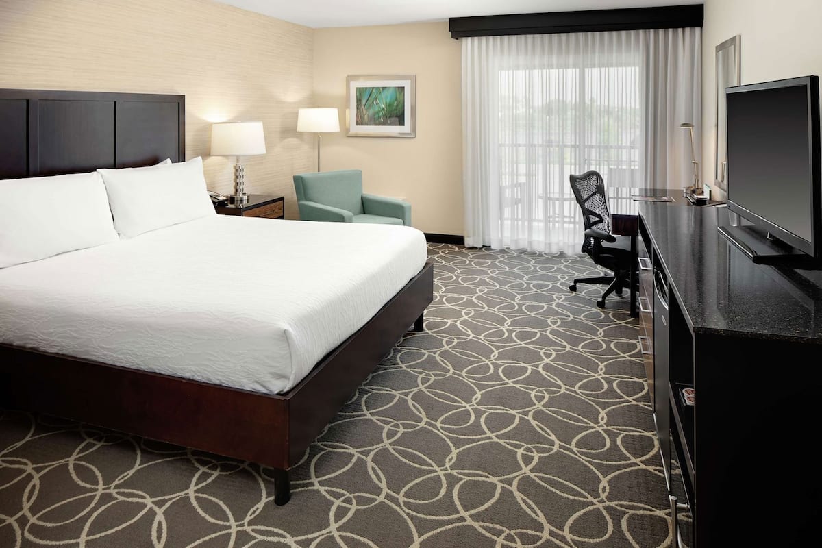 A hotel room with a large bed, a desk with a TV, a chair, and a window with curtains.