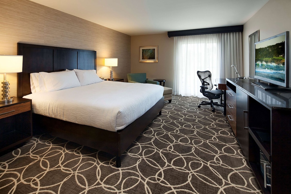 A hotel room with a large bed, a desk with a chair, a television, and a window with curtains.
