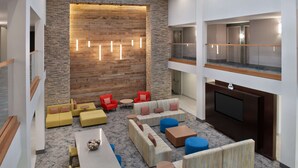 A modern lobby with a stone wall, multiple seating areas, a flat-screen TV, and a glass railing on the upper level. - Hilton Garden Inn Marina Del Rey (Marina del Rey)