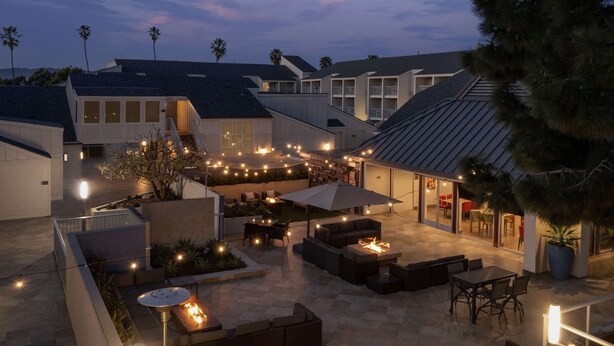 A modern outdoor patio area with seating and a fire pit, surrounded by buildings and palm trees. - Hilton Garden Inn Marina Del Rey (Marina del Rey)