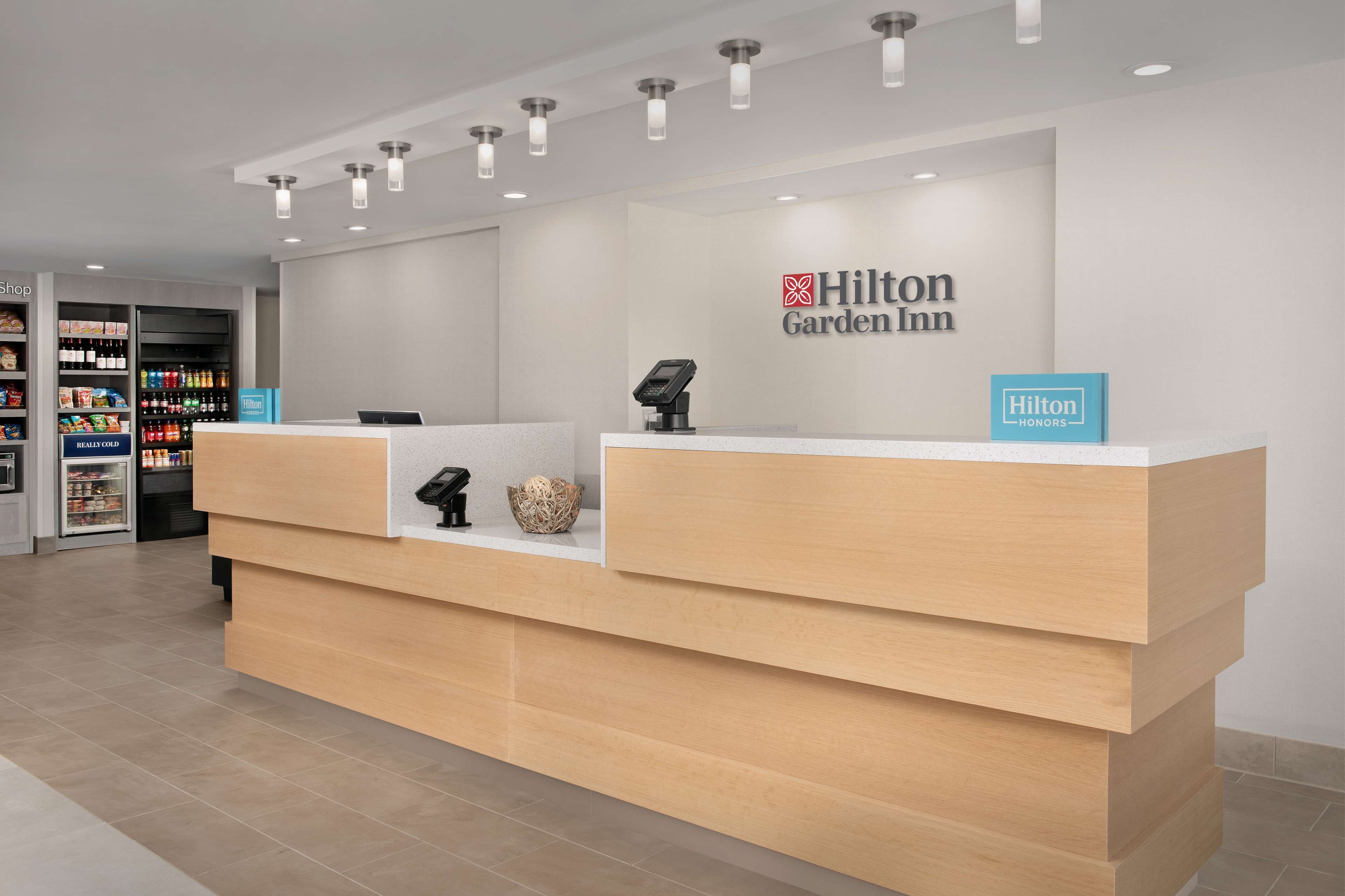 A reception desk at Hilton Garden Inn with a modern design, a self-service kiosk, and a minibar area.