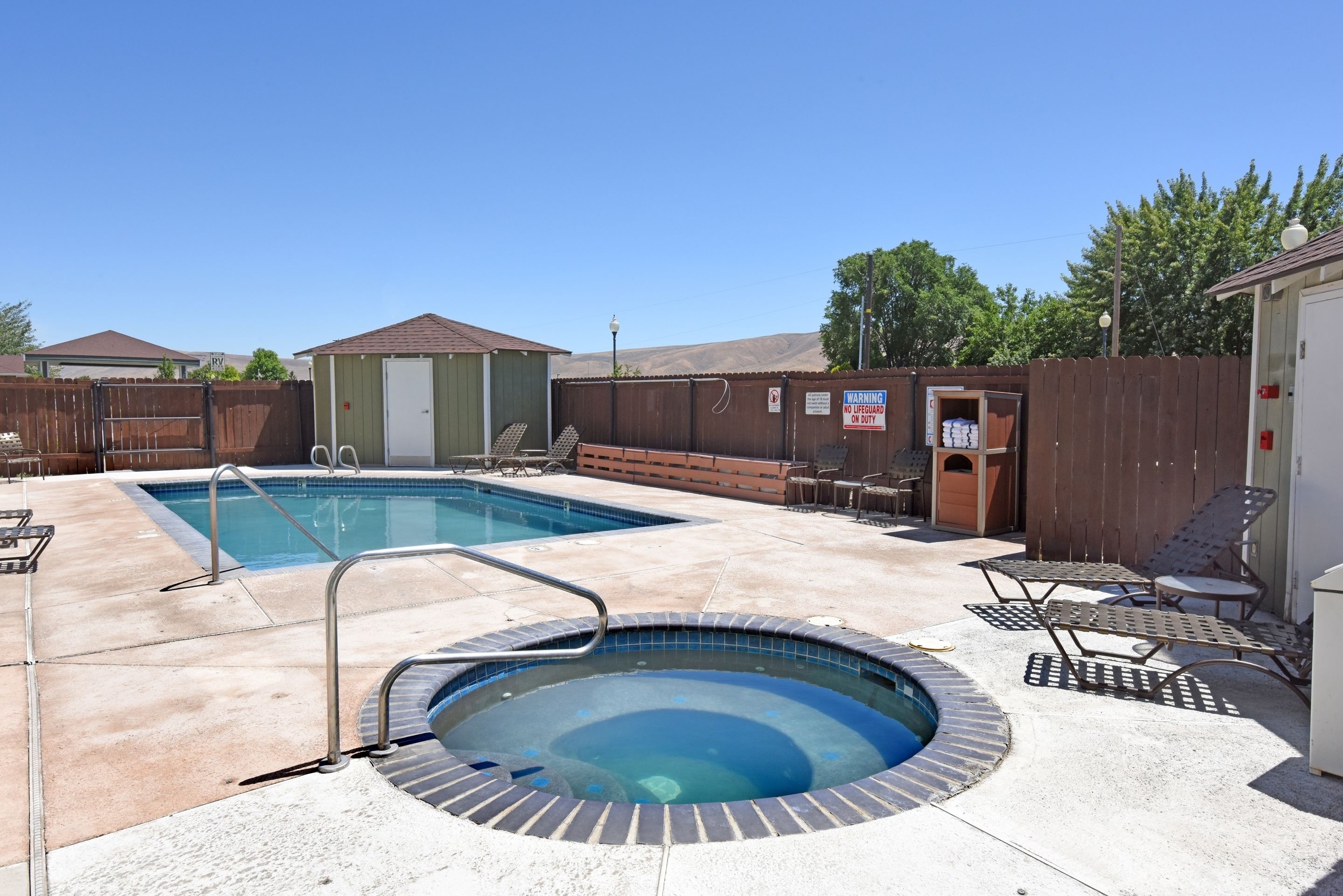 A backyard with a swimming pool, a hot tub, and lounge chairs.
