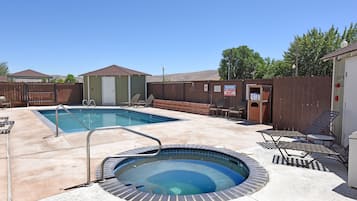 A backyard with a swimming pool, a hot tub, and lounge chairs.