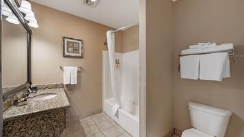 A bathroom with a granite countertop, a white sink, a mirror, a framed picture on the wall, a shower curtain, a toilet, and a towel rack with towels.
