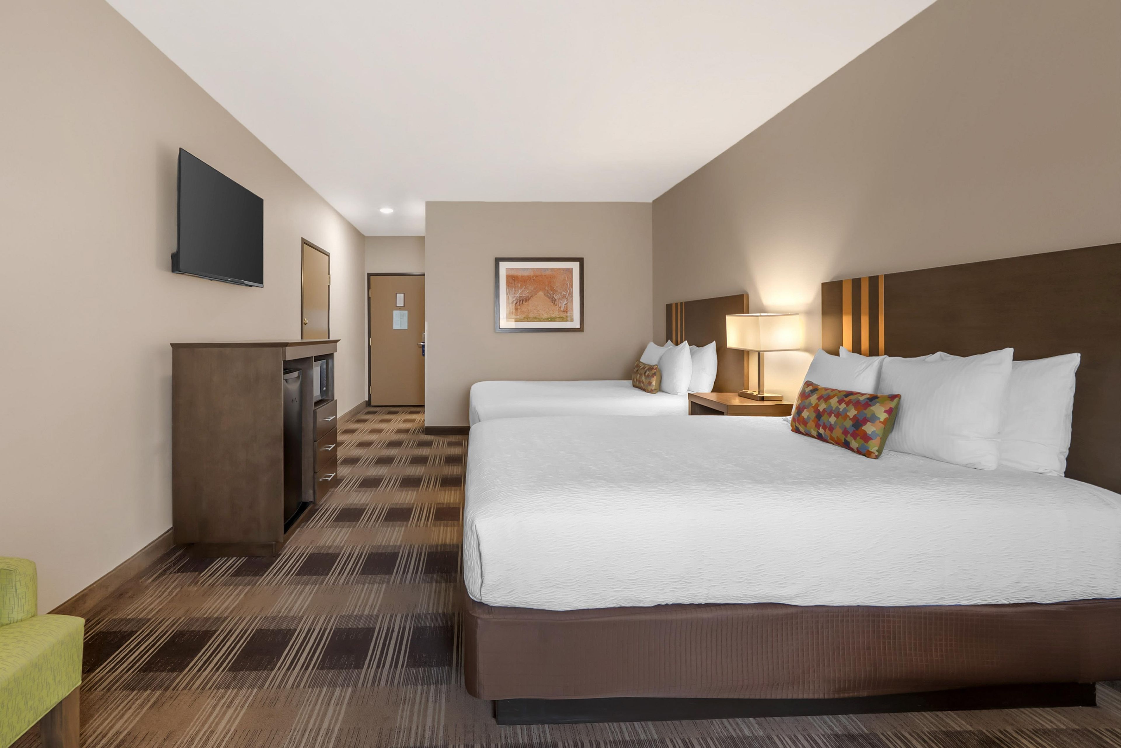 A hotel room with a large bed, a desk, a television, and a framed picture on the wall.