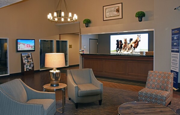 A hotel lobby with a reception desk, two armchairs, a lamp, a television displaying horses, and a framed quote on the wall. - Best Western Plus The Inn at Horse Heaven (Prosser)