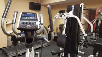 A gym with cardio machines, weight training equipment, and a TV screen.
