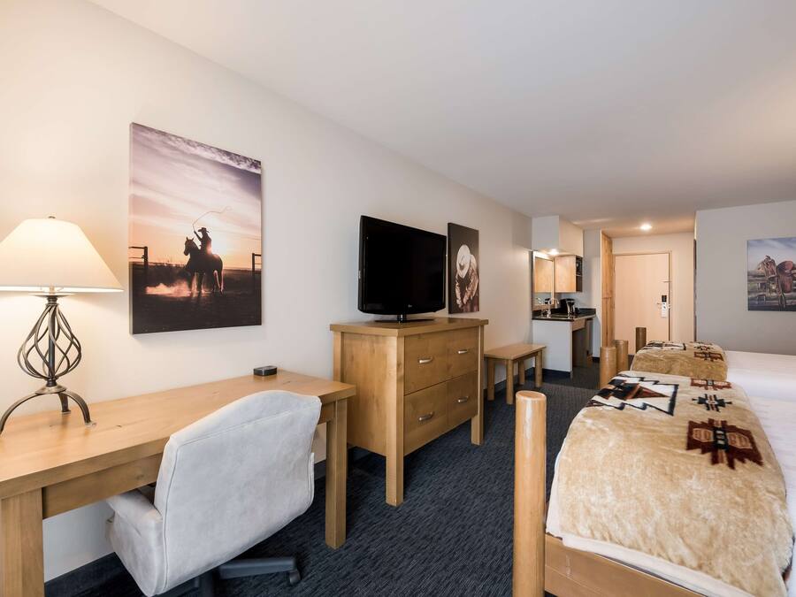 Habitación de hotel con escritorio, silla, cama, televisor y obras de arte en las paredes.