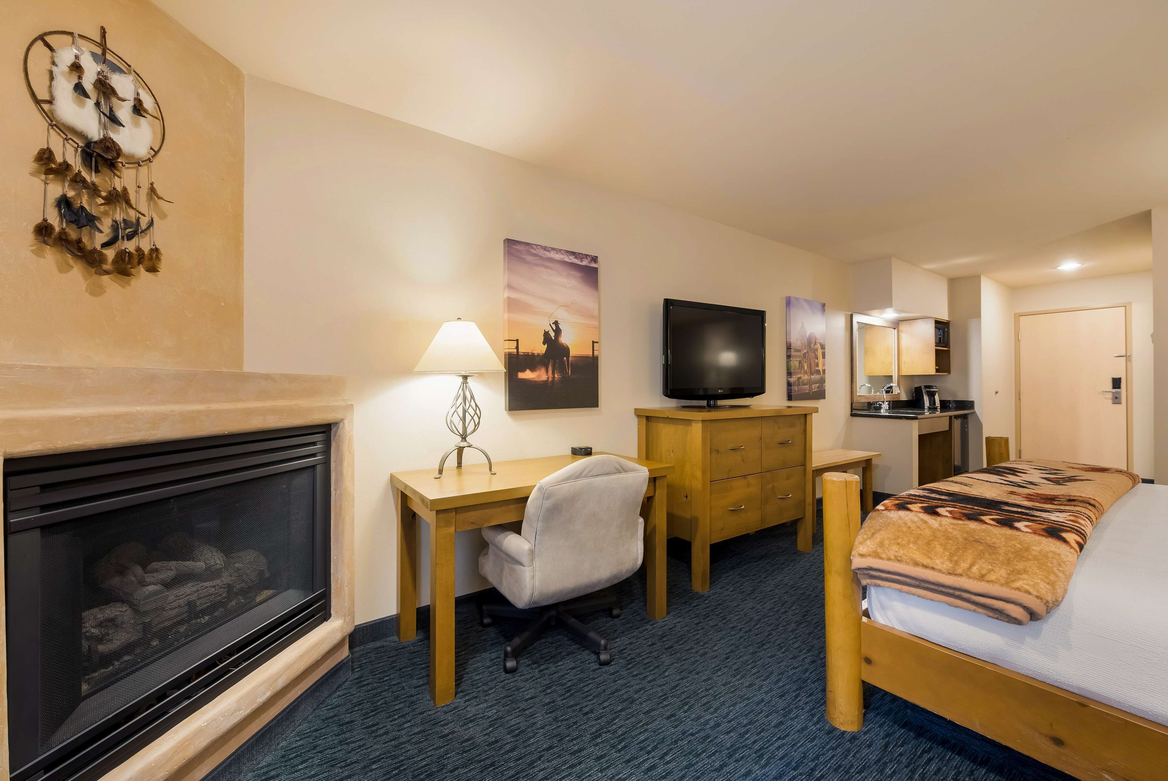 A hotel room with a fireplace, a desk with a chair, a bed with a blanket, a television, and a mirror.