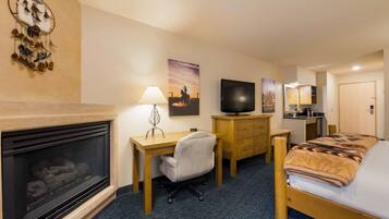 Une chambre d’hôtel avec une cheminée, un bureau avec une chaise, un lit avec une couverture, une télévision et un miroir.