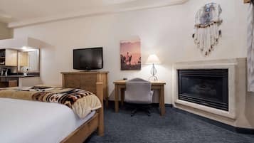 A hotel room with a bed, a desk with a chair, a television, a fireplace, and a wall-mounted artwork.