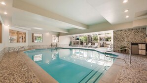 Une piscine intérieure dont le sol et les murs sont recouverts de carrelage en pierre, entourée de chaises longues et d’un mur en pierre.