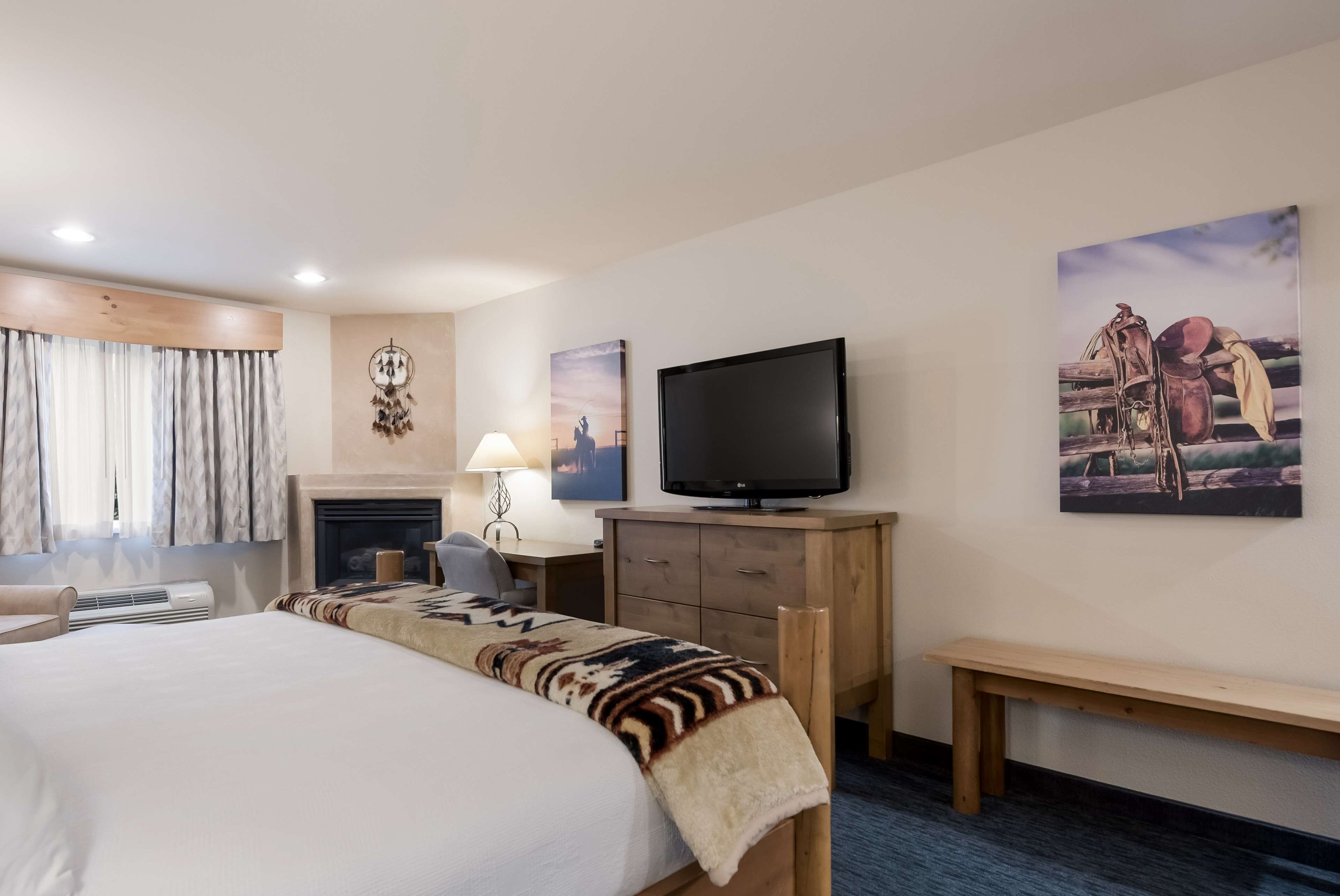 Una habitación de hotel con una cama grande, televisión, escritorio con lámpara, chimenea y obras de arte en las paredes.