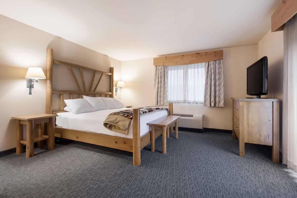 Une chambre d’hôtel avec un lit en bois, des tables de chevet, un bureau, une télévision et une fenêtre avec des rideaux.