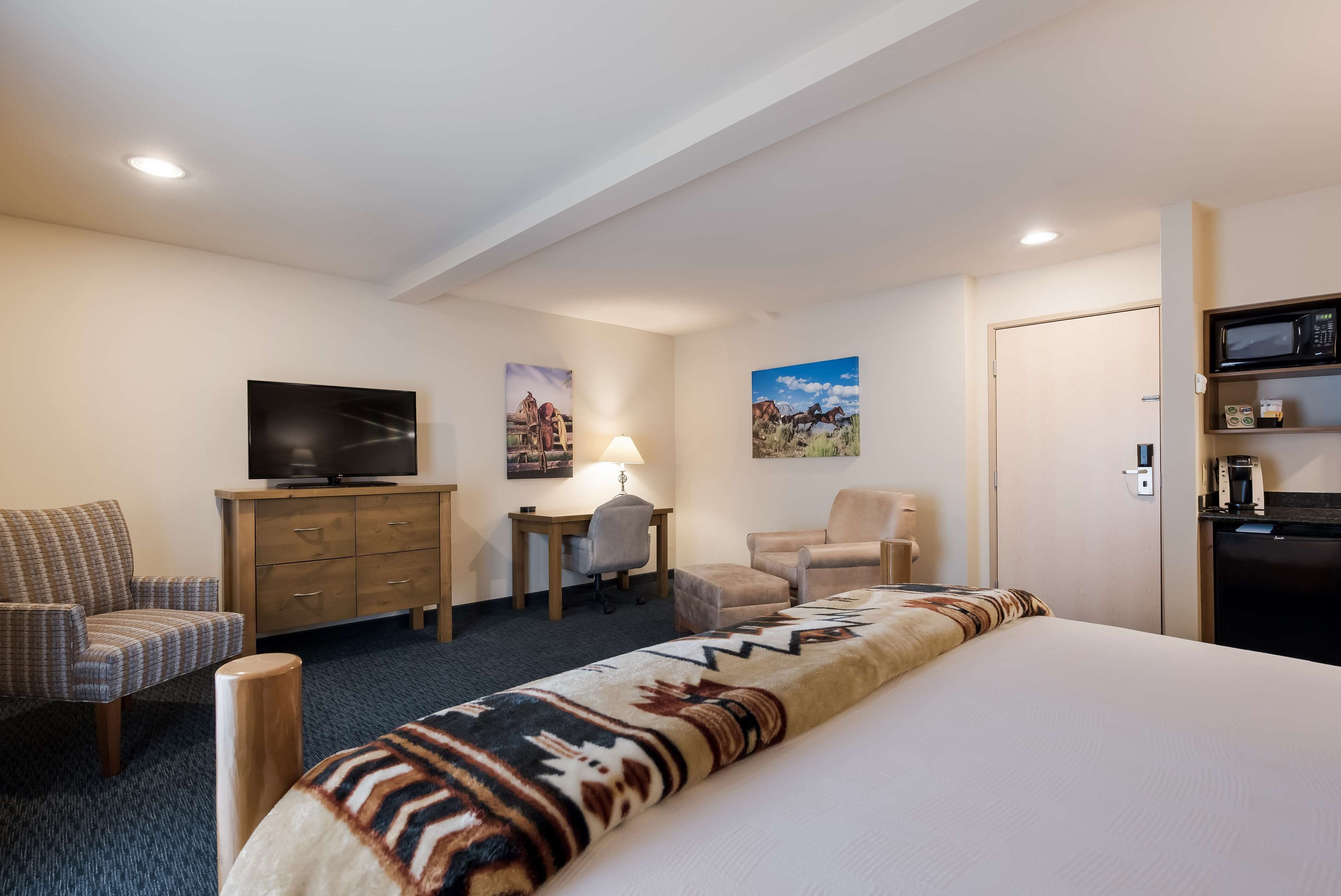 A hotel room with a bed, a television, a desk, and two chairs.