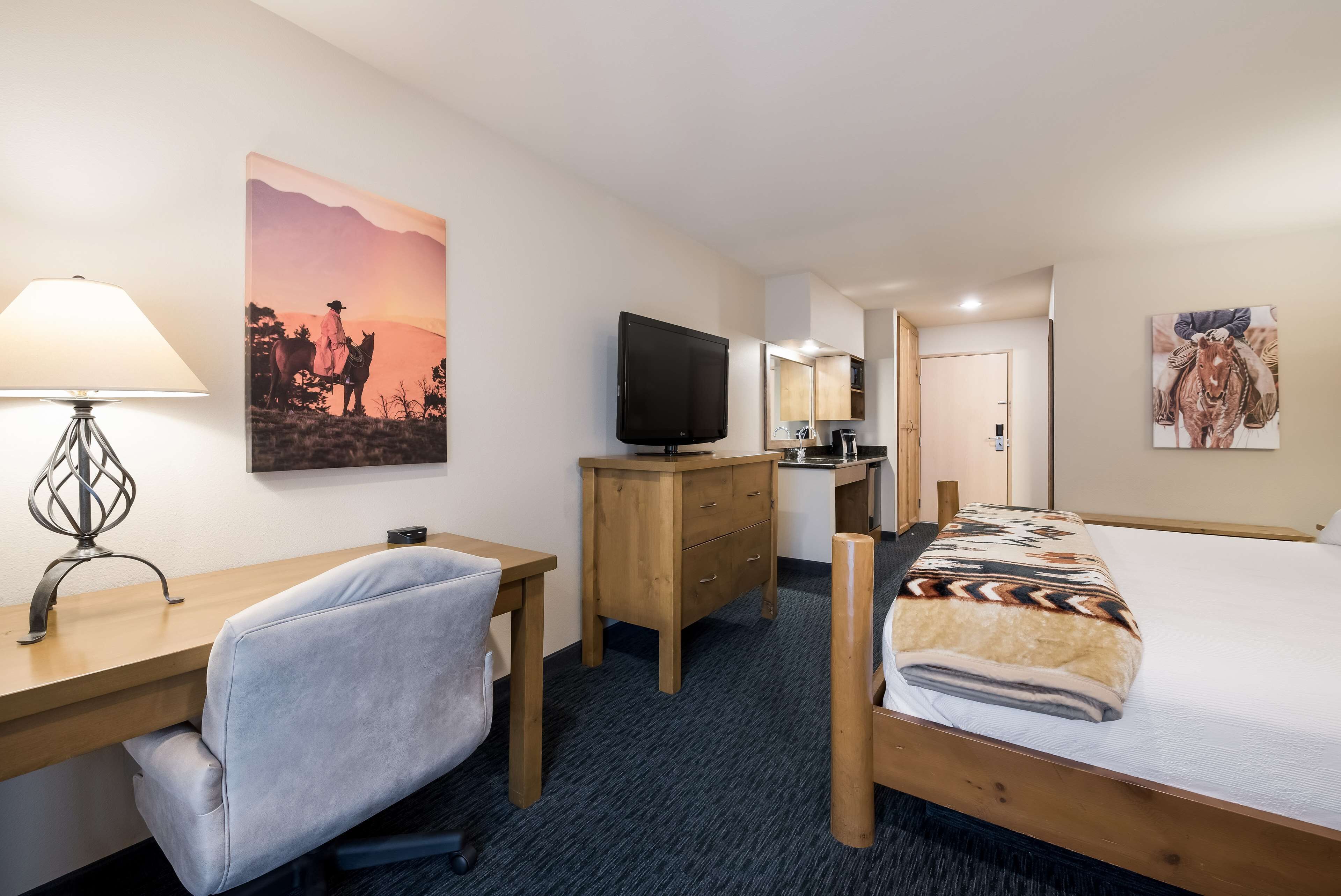 A hotel room with a desk, chair, TV, bed, and artwork on the walls.