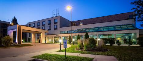 Un edificio moderno con entrada cubierta, fachada de vidrio y señalización que indica estacionamiento reservado.