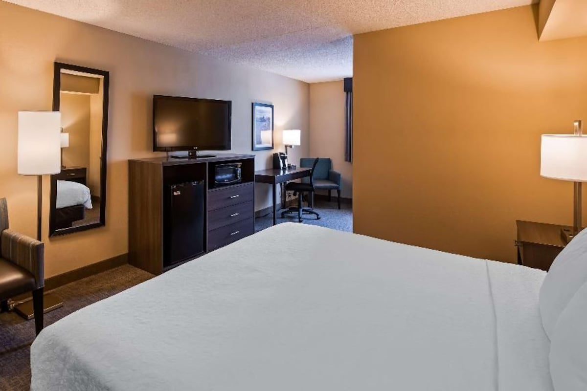 A hotel room with a bed, a desk, a television, a chair, and a dresser.