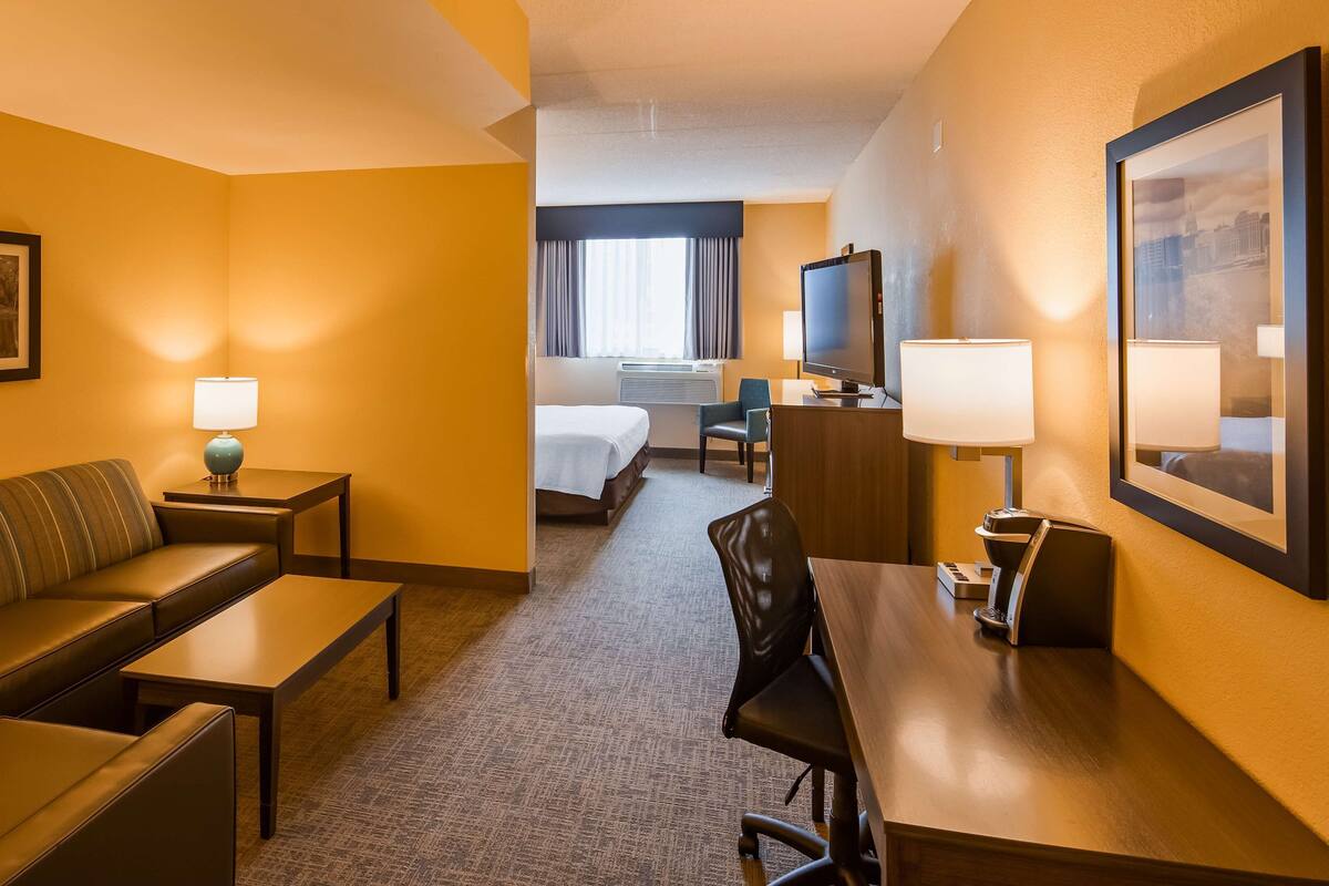 A hotel room with a sofa, a desk, a chair, a bed, a TV, and a framed picture on the wall.