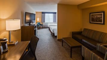 A hotel room with a desk, a sofa, a TV, a bed, and a window with curtains.