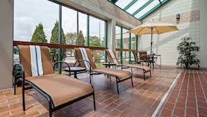 Eine sonnendurchflutete Terrasse mit gepolsterten Sitzgelegenheiten, einem Tisch und einem großen Sonnenschirm.