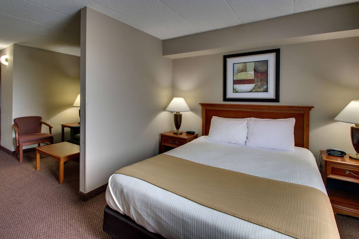 A hotel room with a large bed, two bedside tables with lamps, a chair, and a small table.