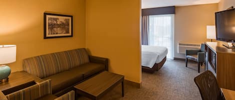 A hotel room with a sofa, a bed, a desk, a television, and a framed picture on the wall.