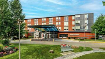 A modern hotel with a covered entrance, a brick facade, and a landscaped front yard.