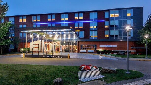 A modern hotel with a glass entrance, a sign reading "WHOTELS," and a blue neon light strip above the entrance. - Aloft by Marriott Lexington (Lexington)