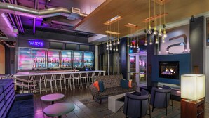 A bar area with a neon sign, seating, and a fireplace. - Aloft by Marriott Lexington (Lexington)