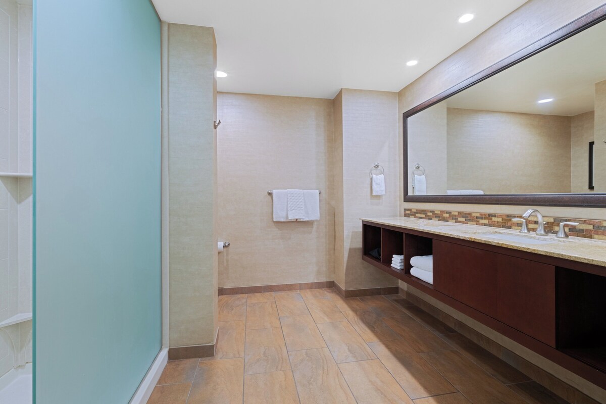 Un baño moderno con un espejo grande, un lavamanos con toallero y una zona de ducha.