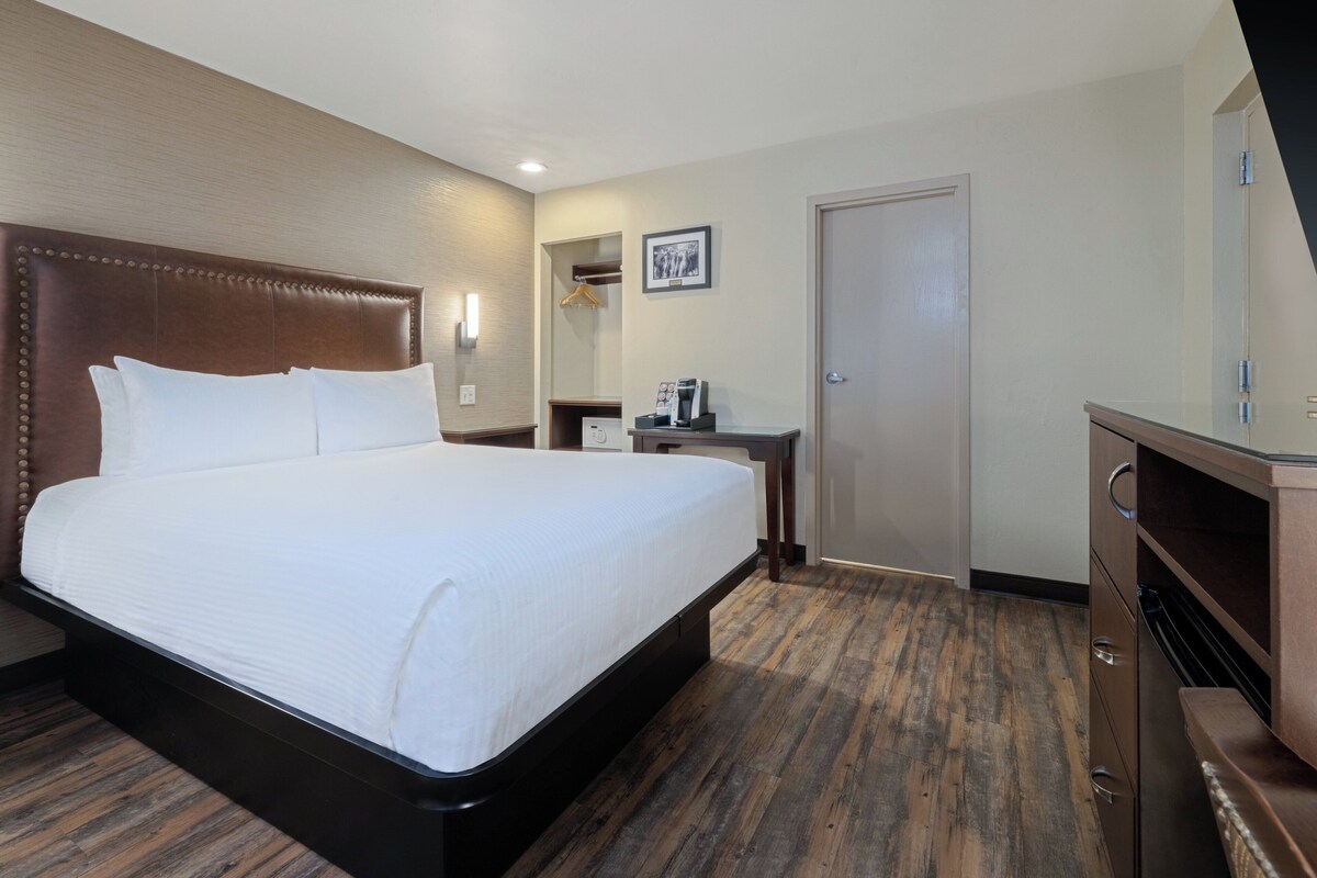 Una habitación de hotel con una cama grande, un aparador de madera, un escritorio con cafetera y una puerta.