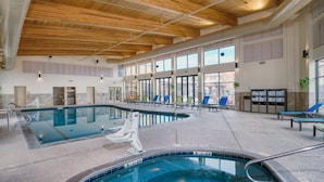 An indoor swimming pool with multiple lanes, lounge chairs, and a wooden ceiling.