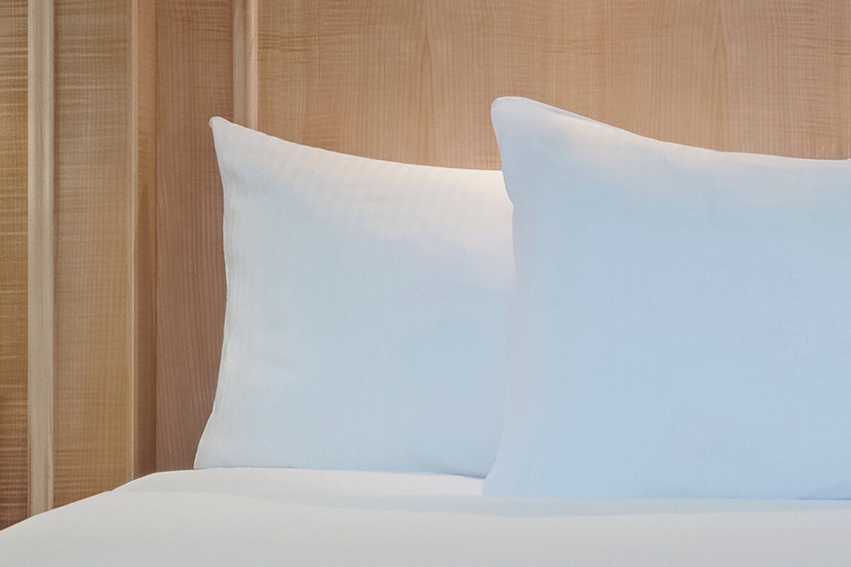Una cama bien tendida con ropa blanca y almohadas frente a un cabecero de madera.