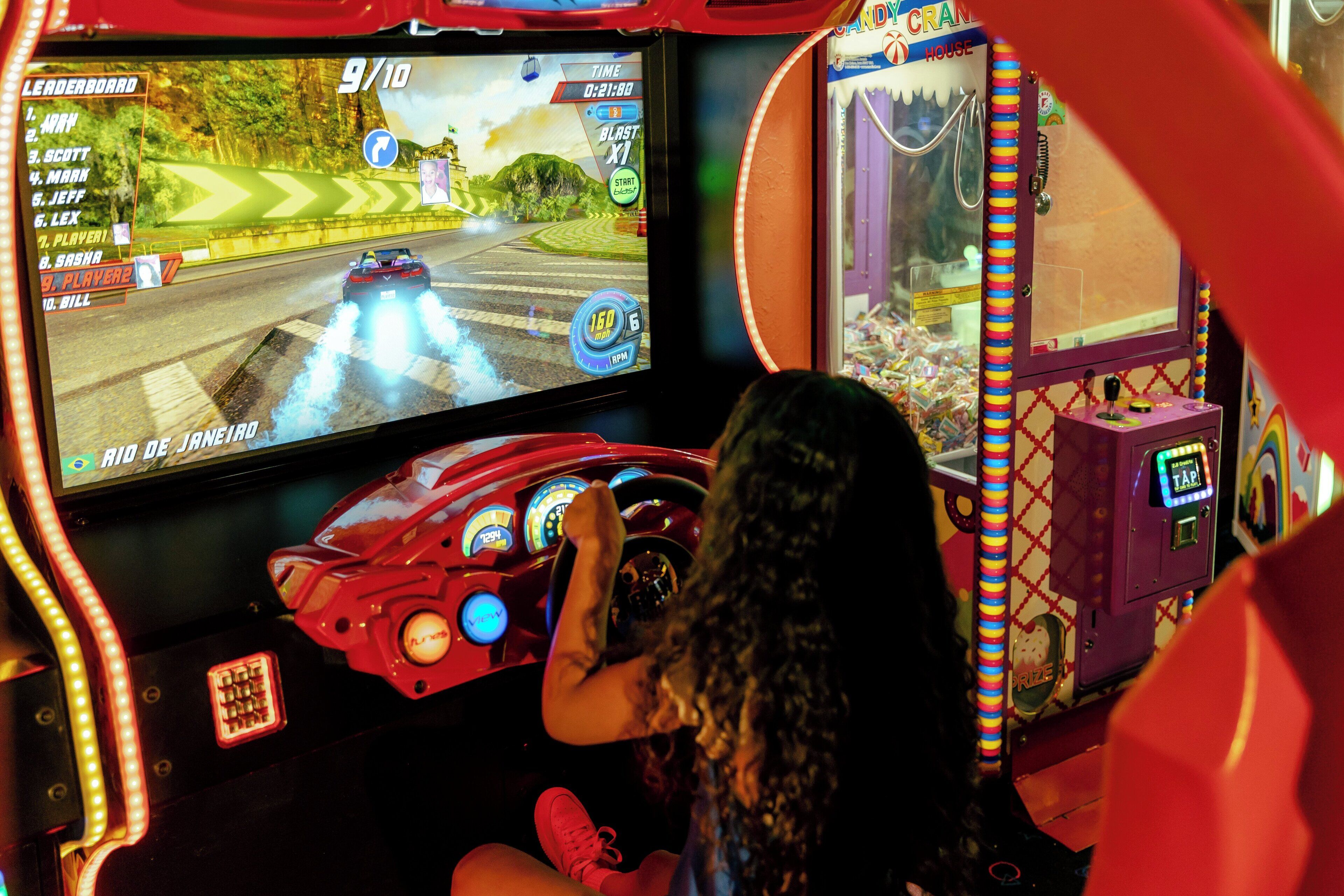 Une personne jouant à un jeu vidéo de course dans une salle d’arcade.