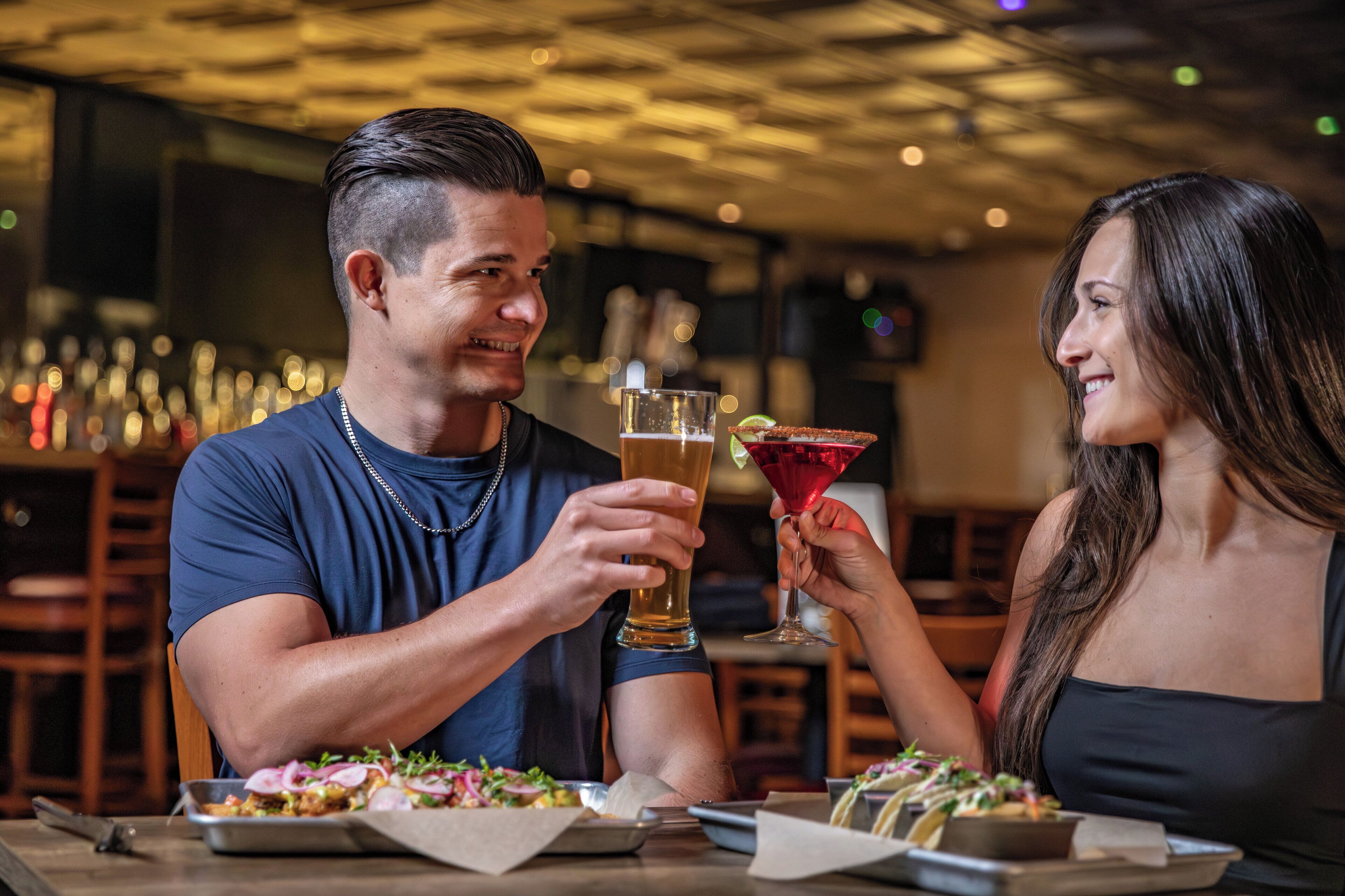 Una pareja sentada a una mesa con comida y bebidas en un restaurante con poca luz.