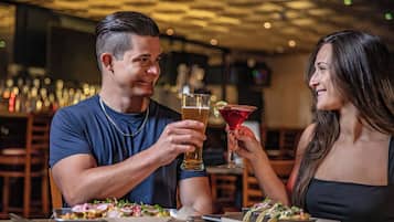 Un couple est assis à une table dans un restaurant à la lumière tamisée, devant un repas et des boissons.