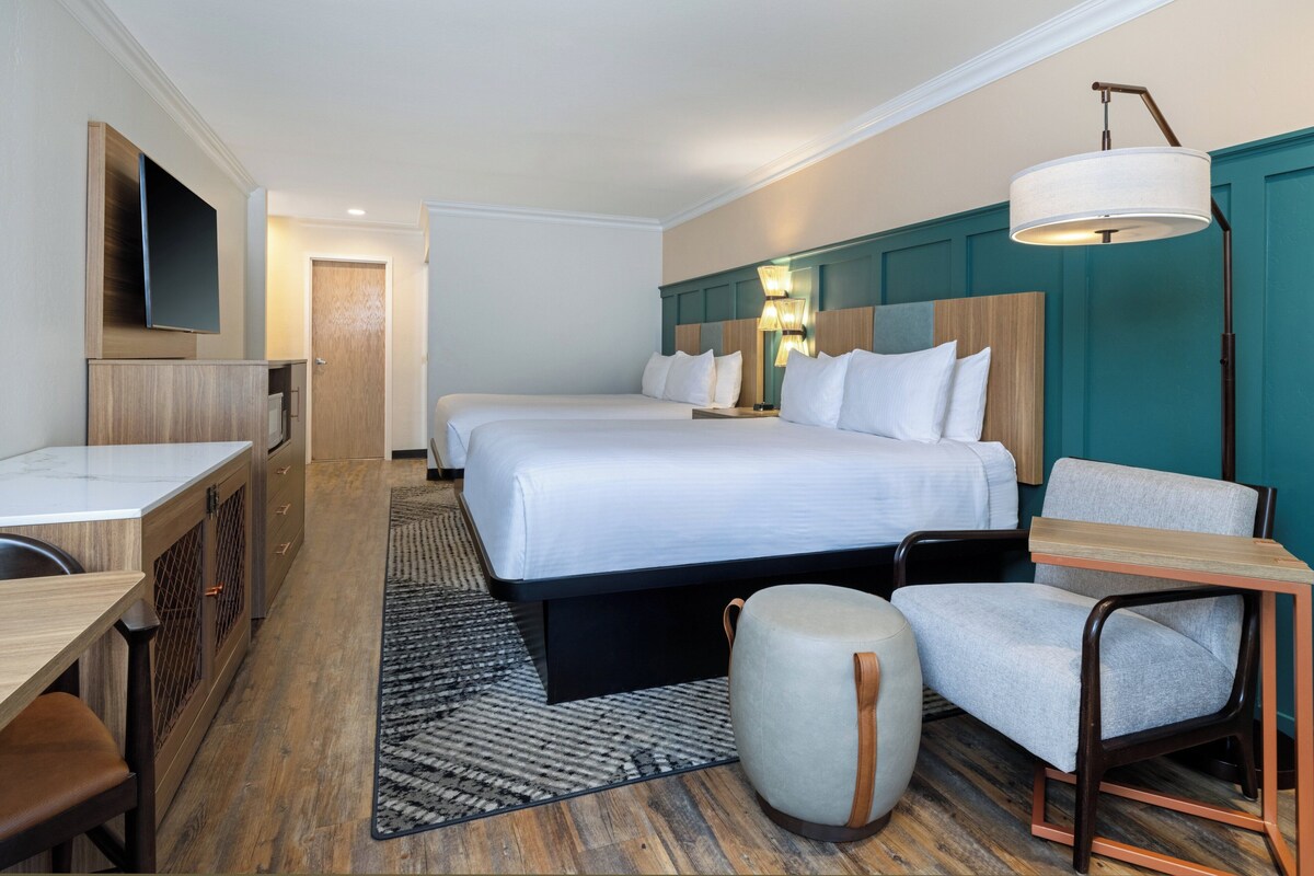 Habitación de hotel con cama, dos mesitas de noche, escritorio, sillón, sofá y televisor.