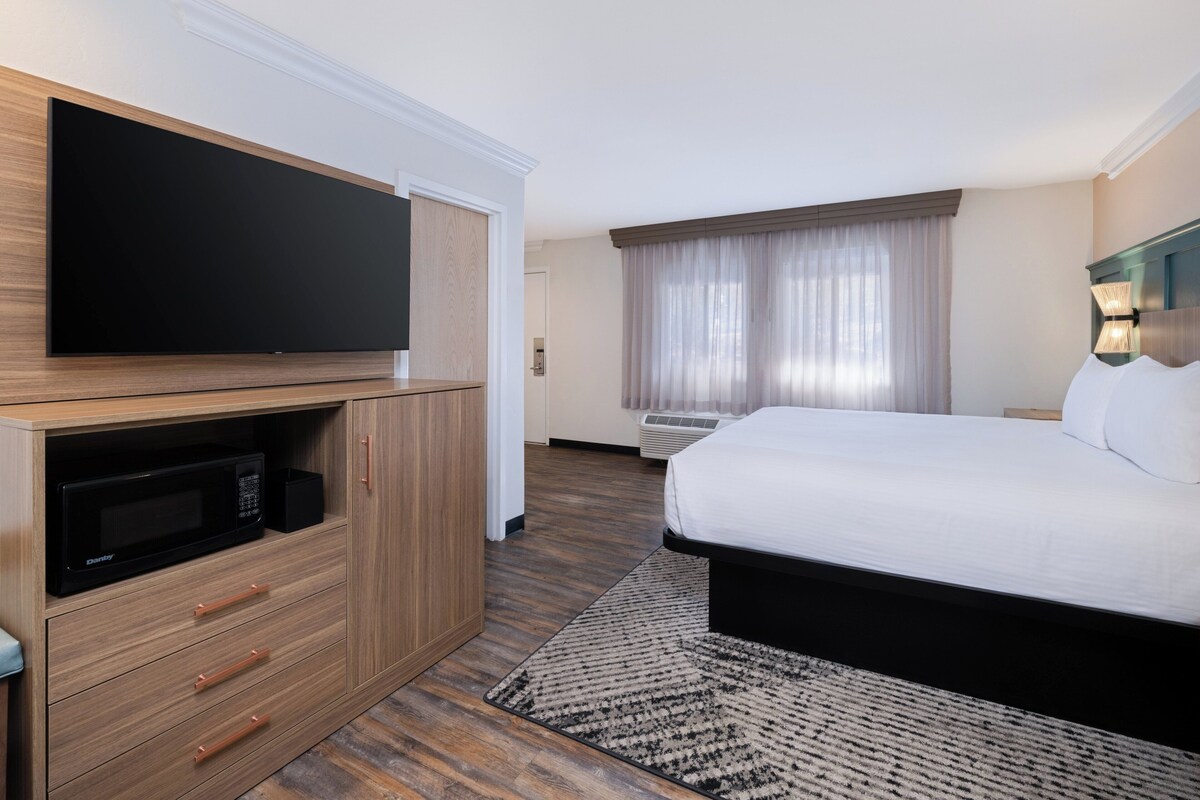 Habitación de hotel con cama, televisor, minibar y ventana con cortinas.