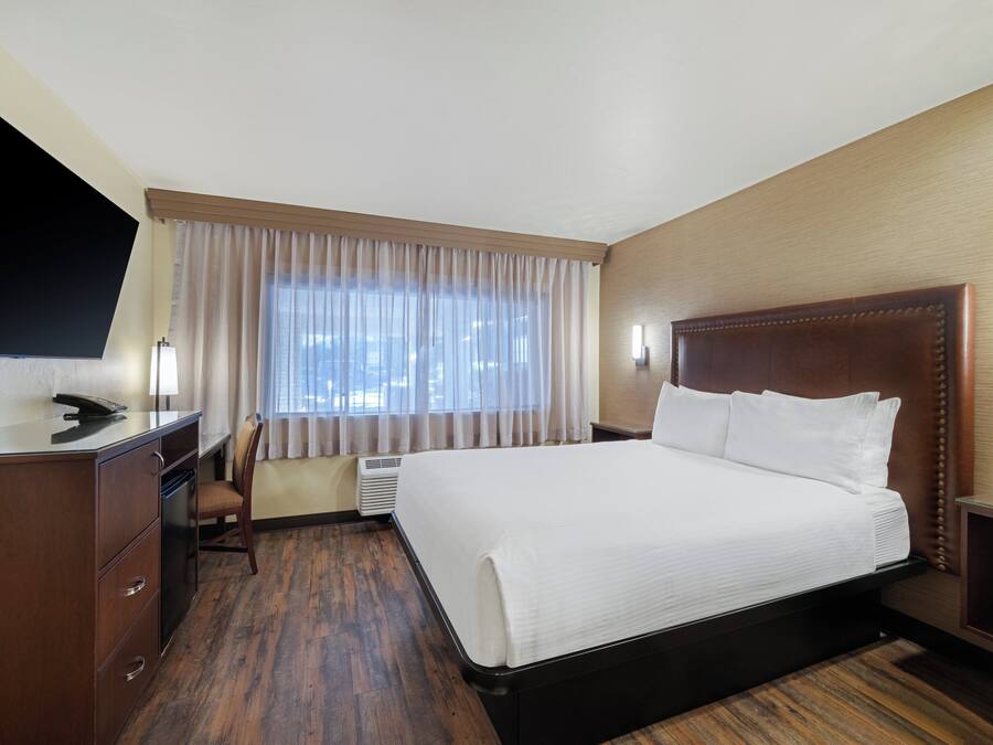 A hotel room with a large bed, a desk with a telephone, a chair, and a window with curtains.