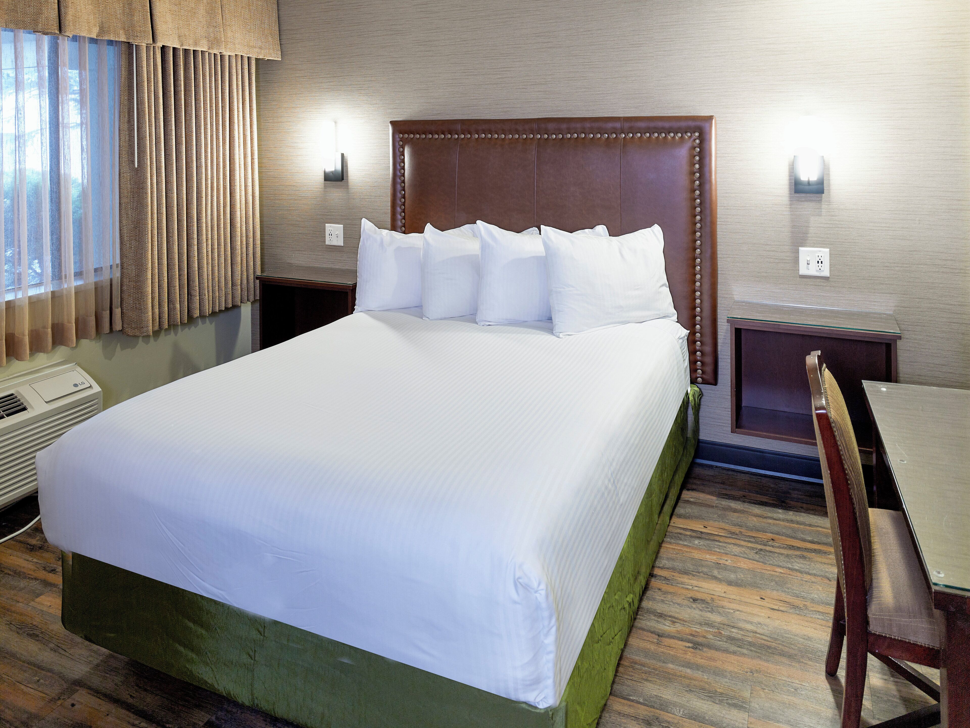 Une chambre d’hôtel avec un grand lit, un bureau, une chaise, un appareil de climatisation et une fenêtre avec des rideaux.